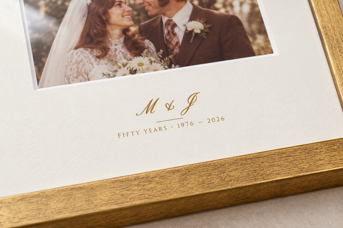 Close-up of the initials M & J and "Fifty years 1976 – 2026" printed in gold-tone ink on the mat