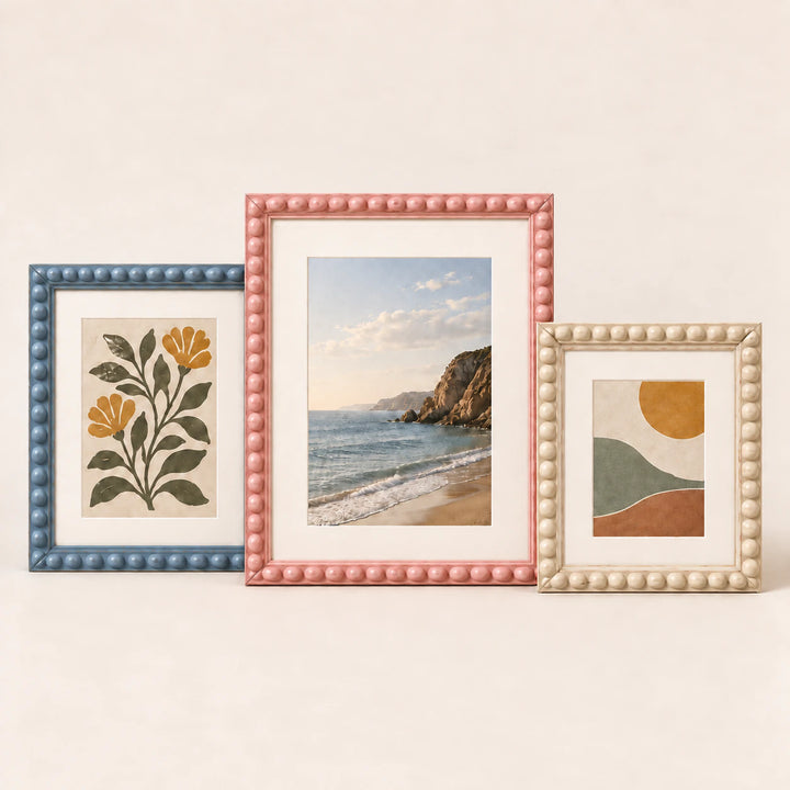 Three painted bobbin picture frames in blue, pink and cream finishes with varied artwork