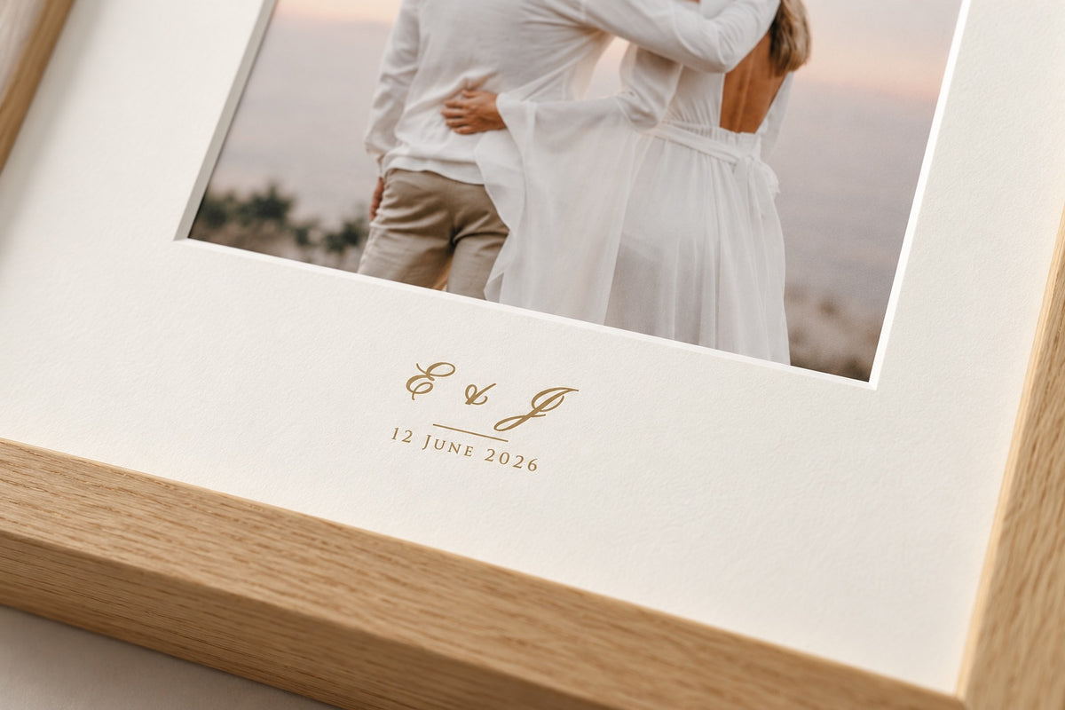 Close-up of a gold-tone monogram and wedding date printed on the mat of an oak frame